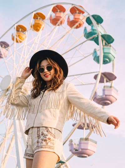 Woman in black hat stands tall before pastel Ferris wheel