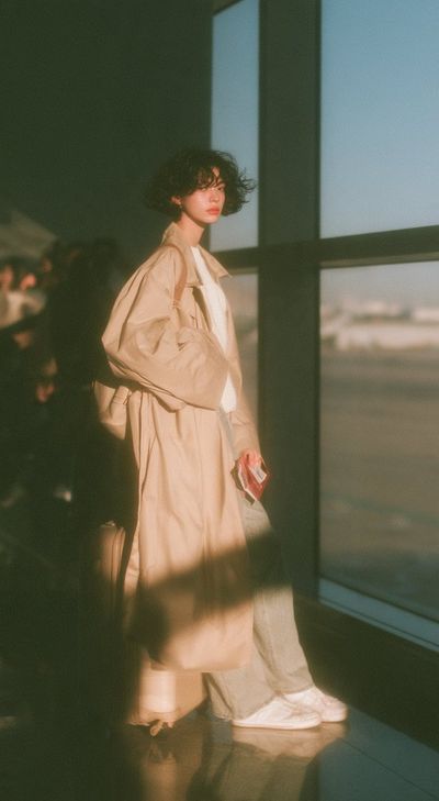 Woman in Trench Coat Pauses by Airport Window at Dawn