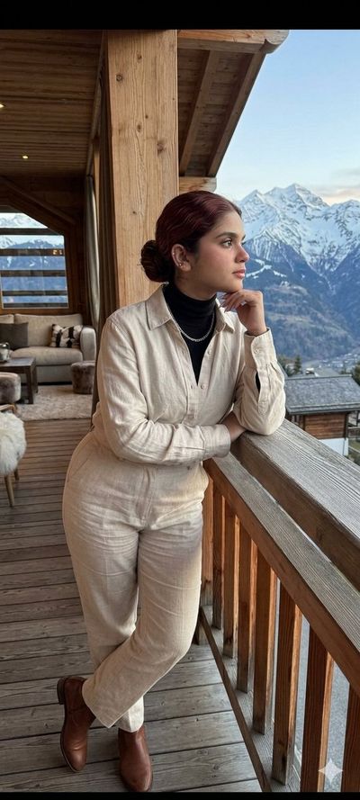Young woman in linen enjoys mountain view from wooden balcony