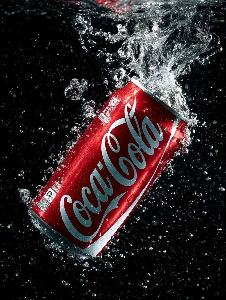 A glossy soda can erupts with water splashes against black background