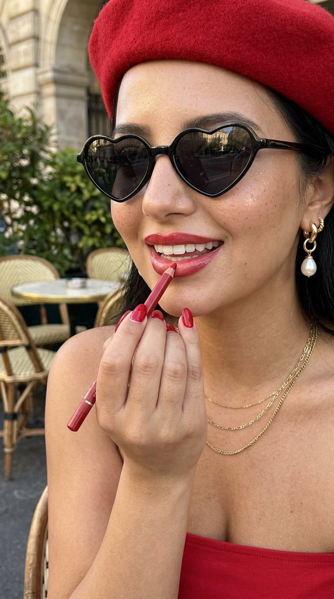 A woman in a red beret applies lipstick at a Paris café