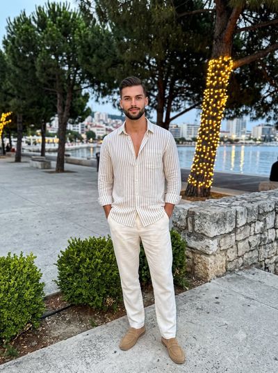 Man in striped shirt stands confidently on evening promenade