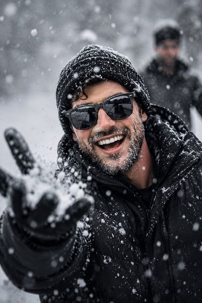 A laughing man in a black beanie throws snow at the camera