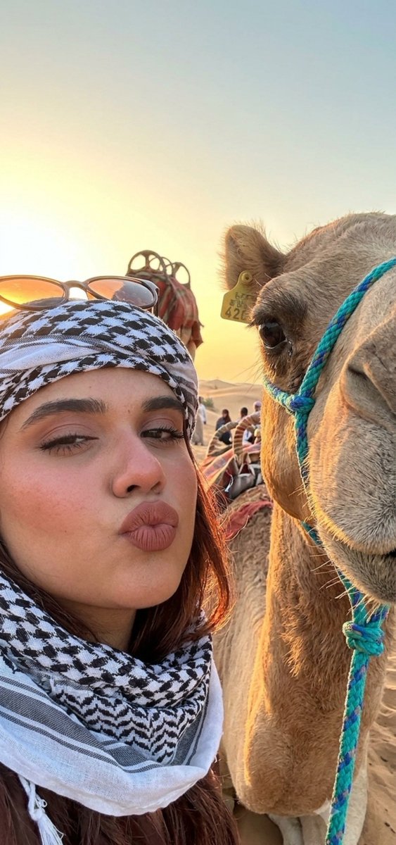 Joyful girl shares a kiss with a camel at sunset