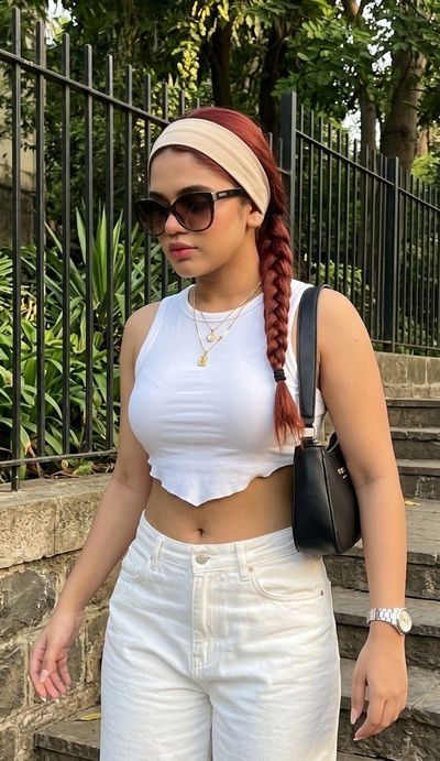 Young woman in white tank top poses by stone staircase in summer light