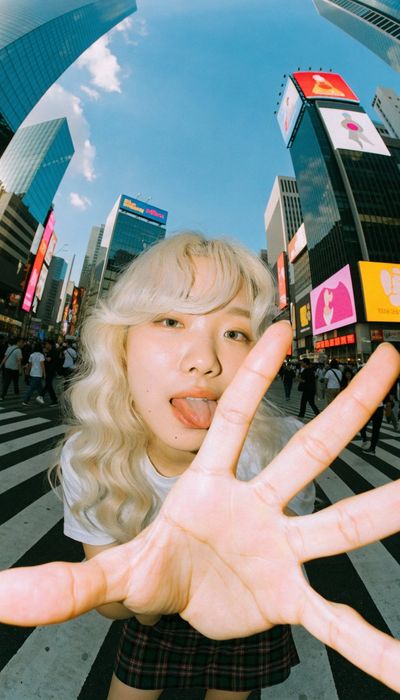 Playful platinum-haired woman reaches toward camera at Shibuya Crossing