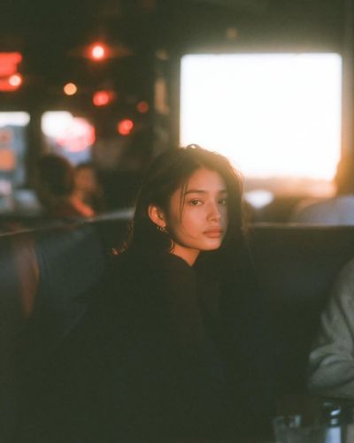 Young woman in dim cafe turns with warm window light across her face
