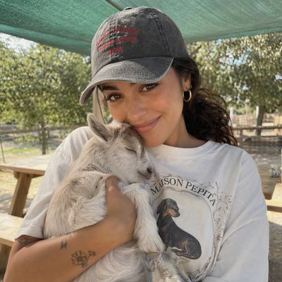 A woman in a cap holds a sleeping baby goat on a sunny farm