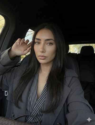 Woman in charcoal trench coat poses serenely inside a car with natural light.