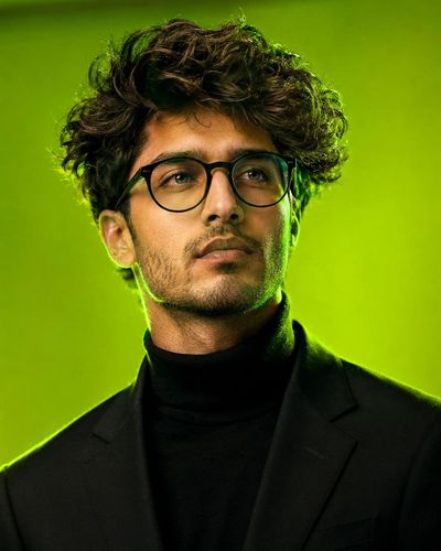 Young man in black blazer stares confidently against neon green backdrop