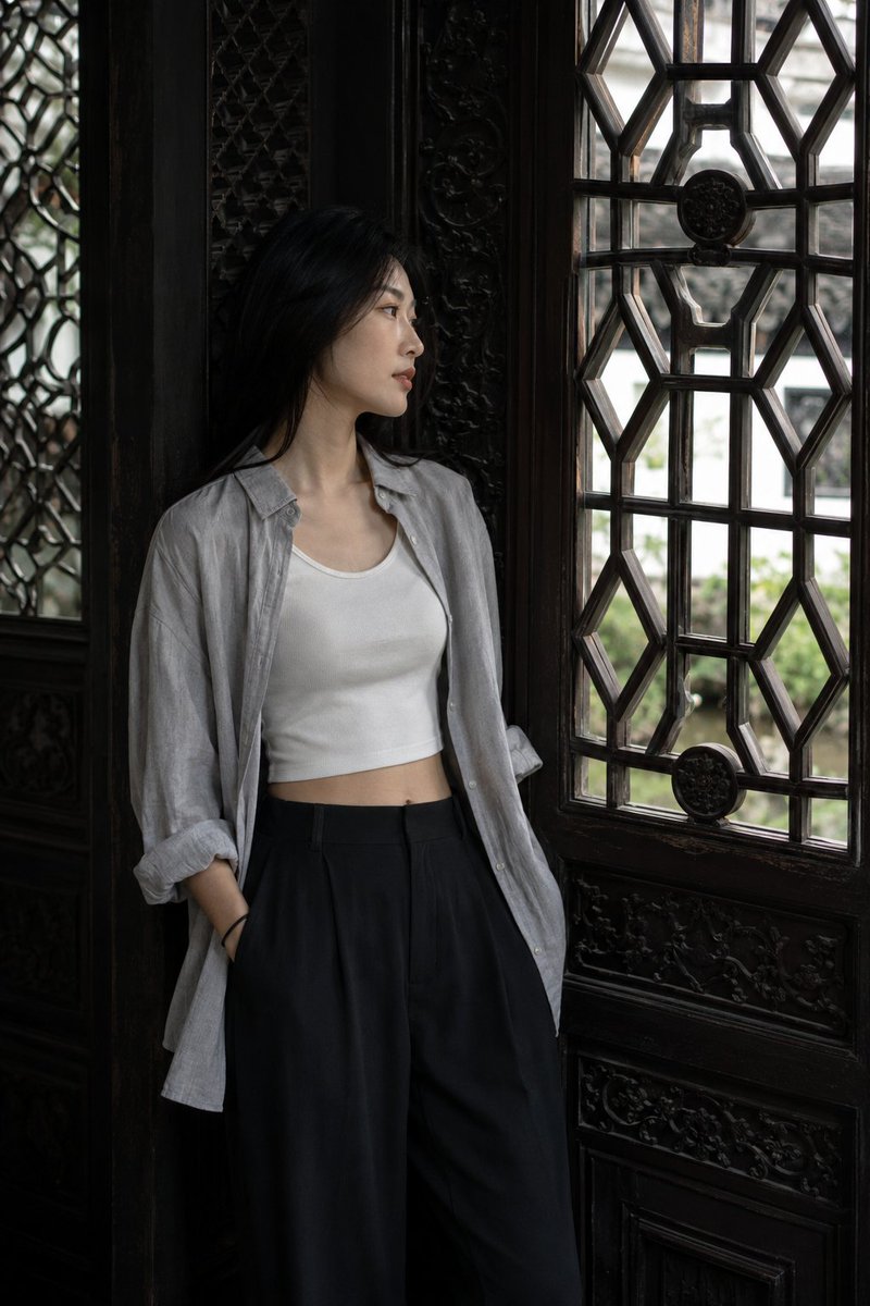 Young woman leans beside carved lattice window in dim hall
