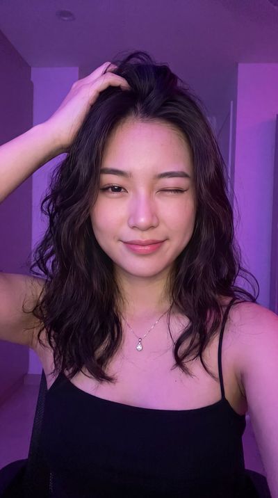 A young woman winks playfully with purple neon light framing her face