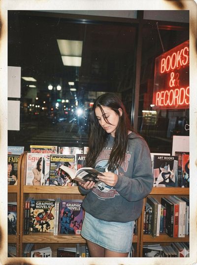 A young woman reads a book in a cozy bookstore at night