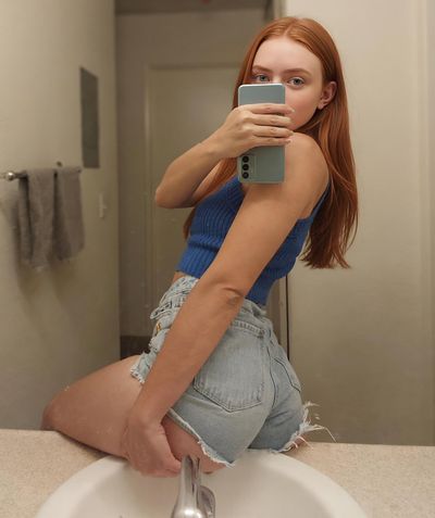 Red-haired woman takes mirror selfie in bright modern bathroom