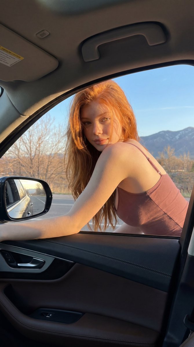 Red-haired woman leans from car window in golden hour light