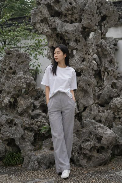 A young woman in white stands before weathered Taihu stones.