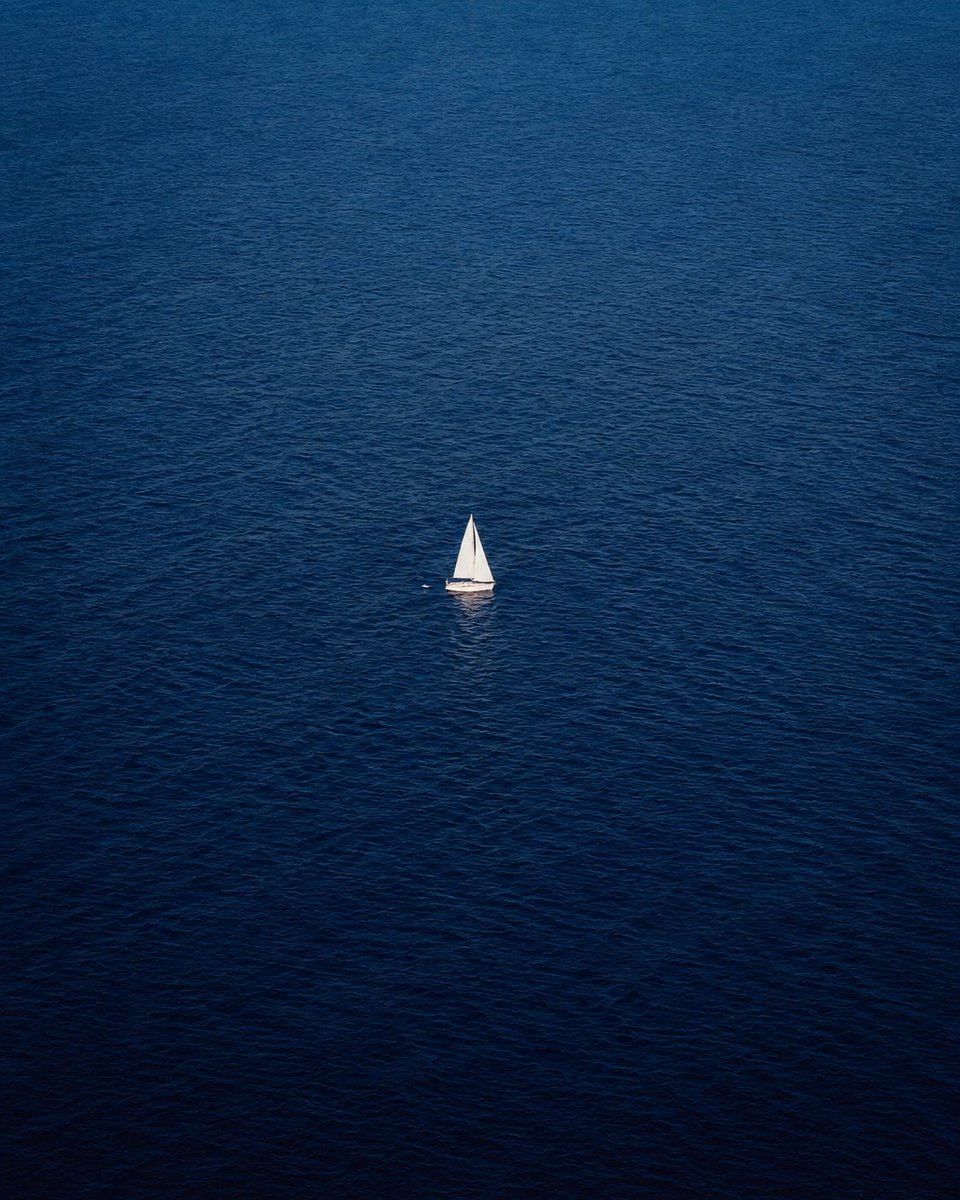 A solitary white sailboat drifts on an endless blue ocean