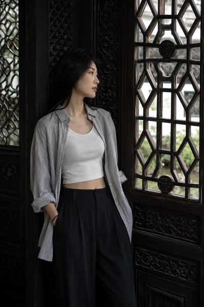 Young woman leans beside carved lattice window in dim hall