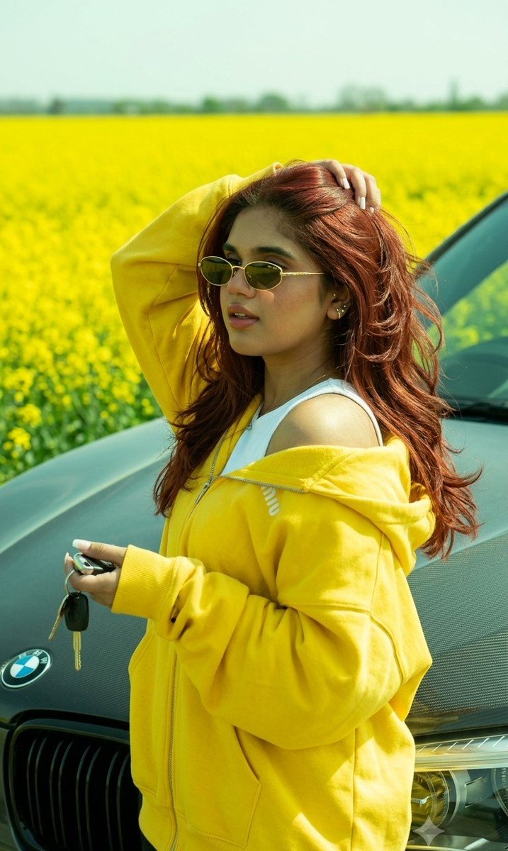 Girl leans against BMW by bright yellow rapeseed field.