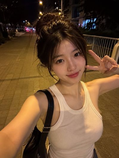 East Asian woman takes a candid night selfie on a quiet sidewalk.
