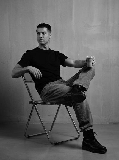 Athletic man sits on chrome chair in monochrome studio