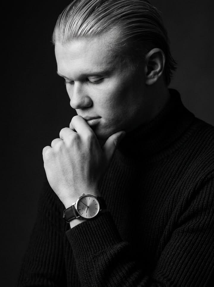 Introspective man in dark knitwear touches wristwatch under dramatic light