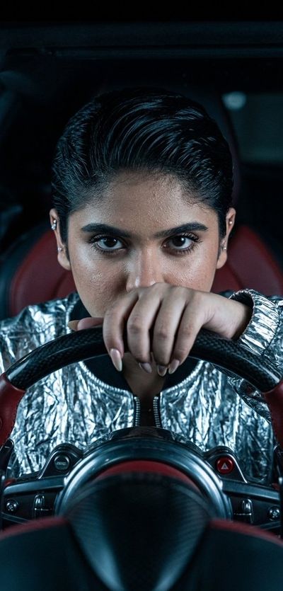A woman with intense eyes grips the steering wheel inside a dark hypercar.