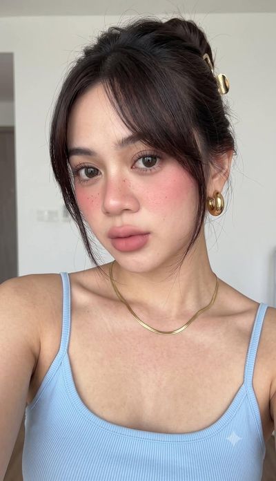 A woman with rosy blush and bangs poses in a bright room