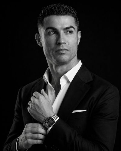 A man in a tailored suit adjusts his watch in dramatic light
