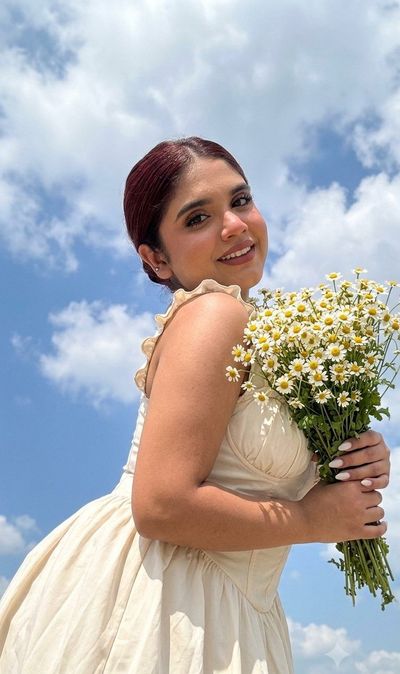 Woman holds daisies under bright blue sky with clouds