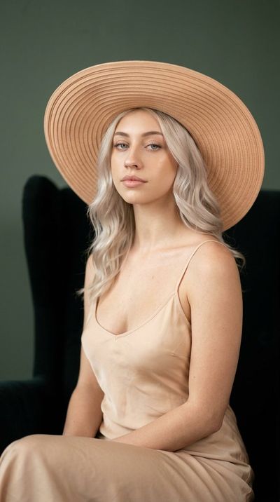 Elegant blonde woman in peach hat sits in teal chair