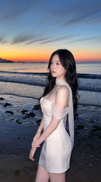 Young woman in white dress poses on beach at blue hour sunset