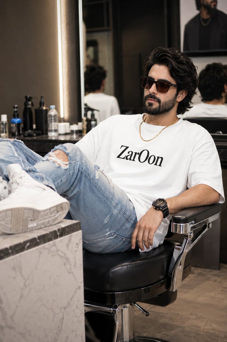Asian man in salon chair wears oversized white tee with ripped jeans