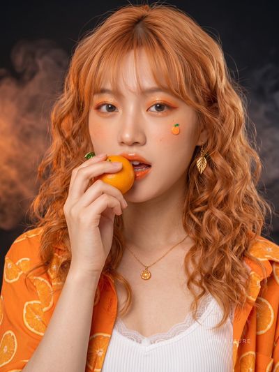 Vibrant orange makeup and curly hair define this close-up portrait