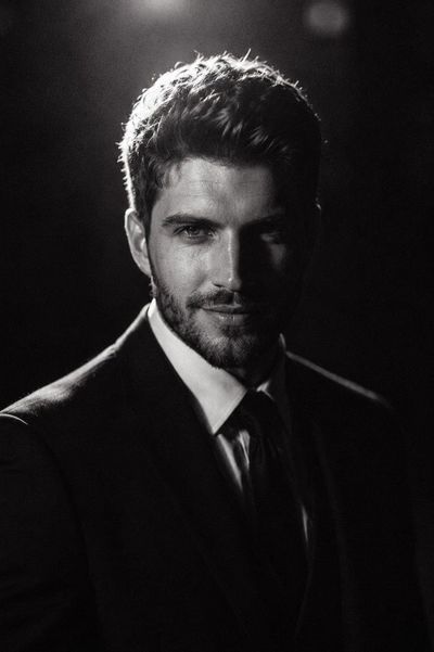A young man in a black suit glows under dramatic low-key lighting.