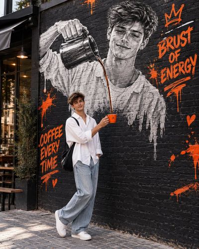 Young man holds orange coffee cup beneath giant mural in urban alley