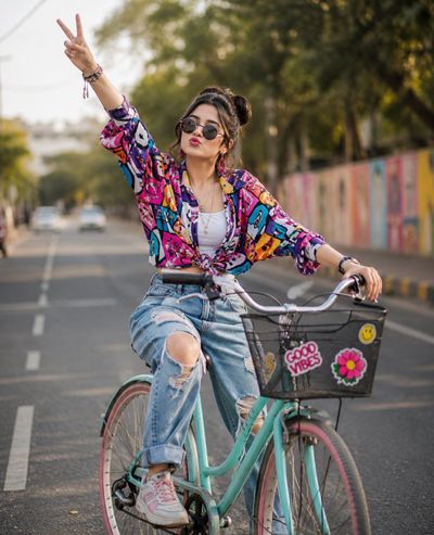 Stylish woman on turquoise bike blows kiss down sunny urban street