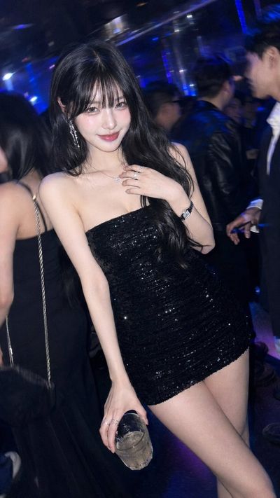 A confident woman in sequined dress poses under neon lights