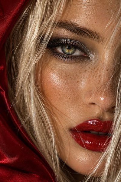 Intense green-hazel eye framed by platinum blonde hair and red hood