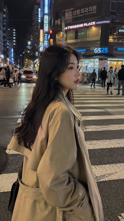 Korean girl crosses neon-lit Seoul street in beige trench coat