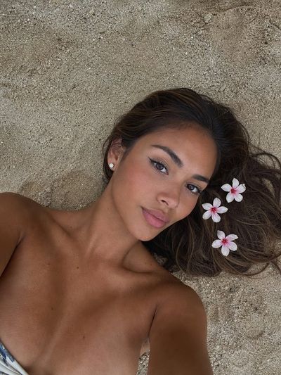 Young woman with tropical flowers lies on warm beach sand