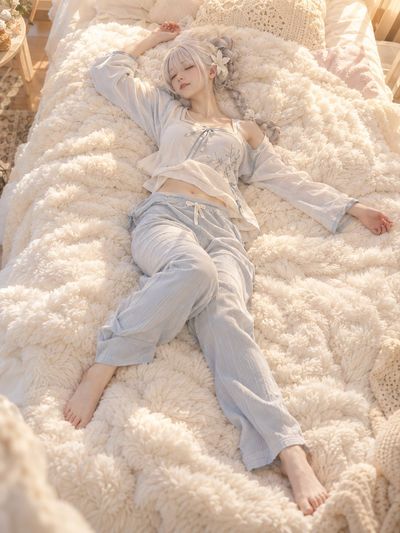 An adult woman lies on a cream blanket in soft morning light
