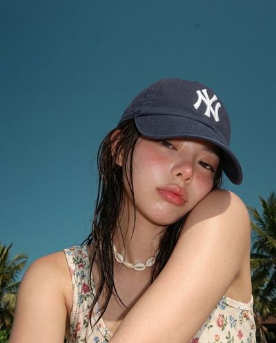 A sleepy girl in a Yankees cap rests under a teal sky