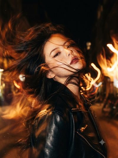 Woman's face emerges from fiery hair in amber night light