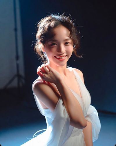 Young Asian bride smiles in beaded gown under dramatic studio lights
