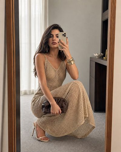 Woman in crochet dress squats for mirror selfie in luxury dressing room
