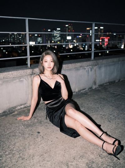 Woman in black velvet poses under hard flash on a rooftop at night.