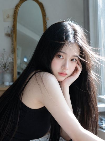 Young woman with silky black hair rests her head in soft sunlight