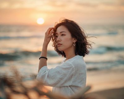 Sunset breeze stirs dark bob as she gazes at glowing horizon