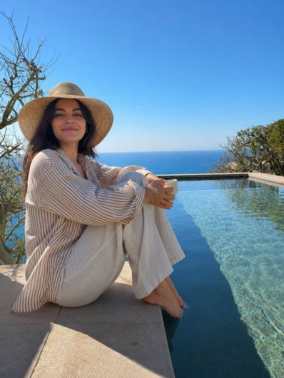 Young woman with straw hat enjoys coffee by infinity pool